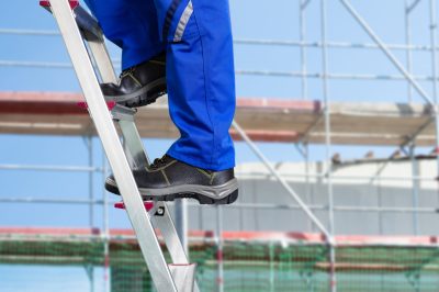 Close-up Of A Handy Repair Man Standing On Steel Ladder Against Construction Sites